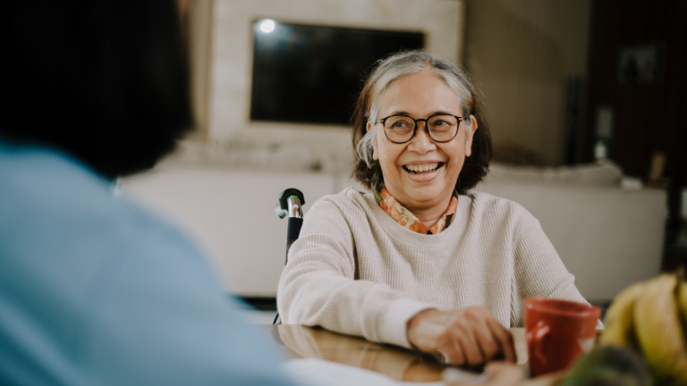 grandmother with grey and black hair and white long sleeve smiling in wheel chair after being sponsored